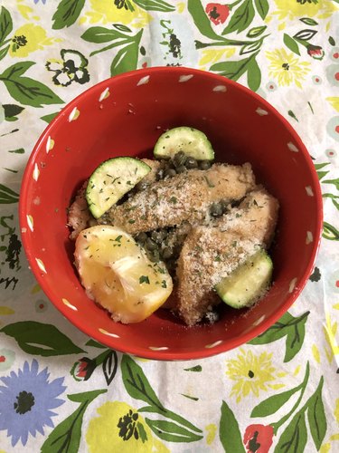 chicken piccata in a red dish on floral tea towel