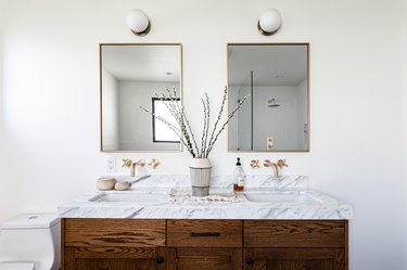 wood bathroom vanity with white stone countertop, double sinks, two mirrors with gold trim, two sphere white light fixtures