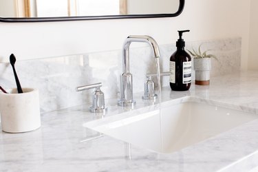 marble vanity countertop, silver faucet, mirror with black trim, toothbrush holder