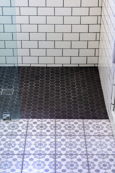 glass shower door, white subway tile wall with black grout, black hexagon tile floor in shower, purple and white floral design on square floor tiles