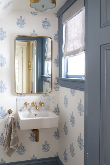 blue and white bathroom under stairs with wall-mounted sink and brass fixtures