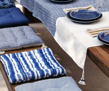 outdoor table with seat cushions, linens, and blue plates
