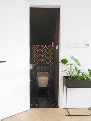 Bathroom under stairs with black tile and a gold chevron wall