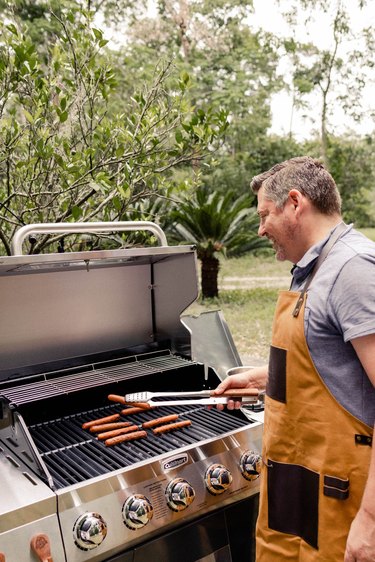 Man grilling hot dogs at Cuisinart grill wearing tan and leather Pit Boss apron