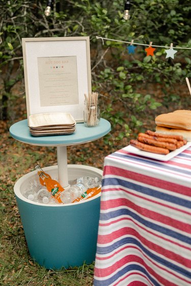 Framed hot dog bar menu on top of blue cooler that also serves as a cocktail table