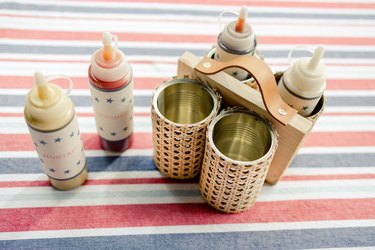 DIY condiment caddy made from four soup cans wrapped in cane webbing and attached to board with handle