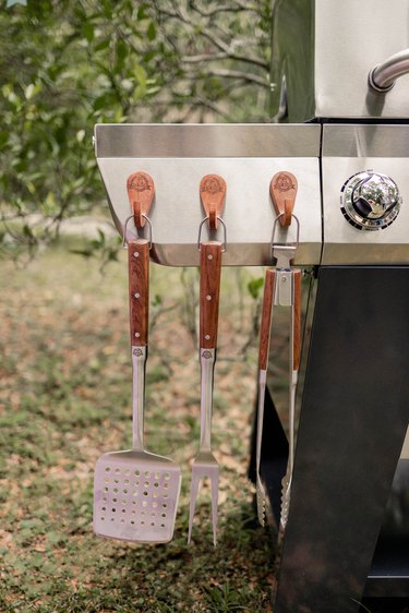 Three wooden Pit Boss magnetic hooks hanging from grill with BBQ tools hanging from them