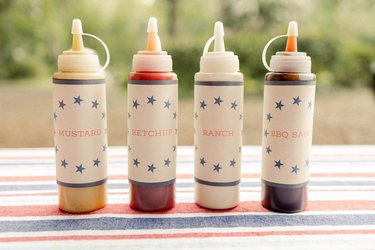 Four hot dog bar condiment bottles with printable labels for mustard, ketchup, ranch, and BBQ sauce