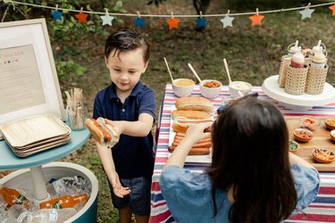 Small boy assembling a hot dog in a bun at the hot dog bar