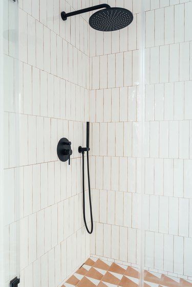 glass shower door with white vertical tiles, black shower head and fixtures, tile floor with orange triangular pattern