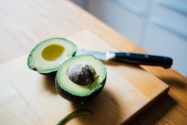 open avocado on cutting board with knife nearby