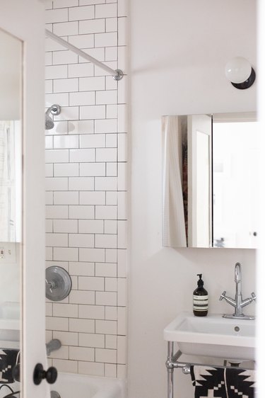 white ceramic console sink, mirrored medicine cabinet, white subway tile shower wall, round white light fixture