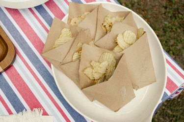 Potato chips in small brown bag pouches inside serving dish