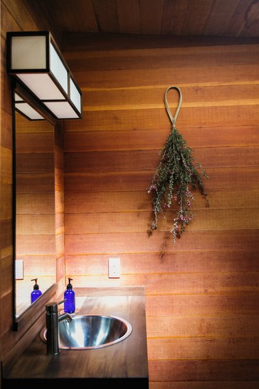 wood panel walls, wood bathroom countertop, stainless steel sink, rectangular mirror, hanging greenery