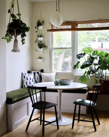 Kitchen nook idea with white tulip table and black bistro chairs in a kitchen nook with lots of plants