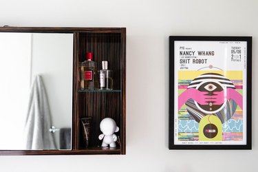 wood surface-mount medicine cabinet with beauty products inside, framed concert poster