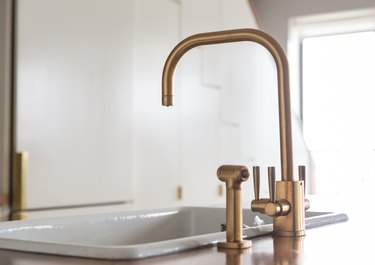 gold faucet mounted next to cast iron sink