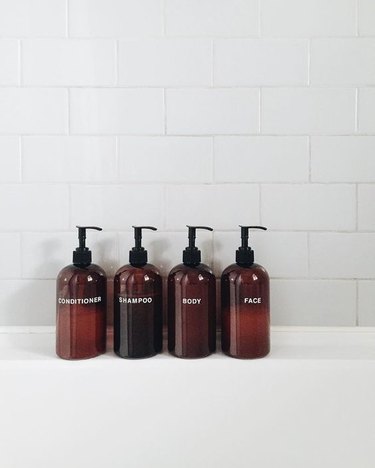 spa bathroom ideas featuring four amber-colored product dispensers lined up along a bathtub with white tile