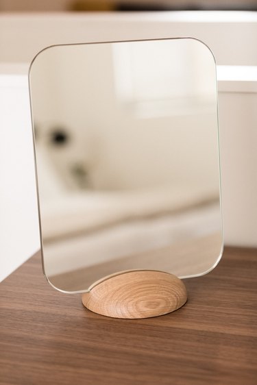 minimal table mirror with light wood base on a dark wood console