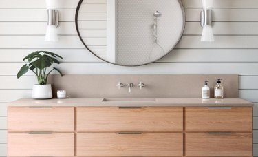rose quartz countertop colors with natural wood cabinets, integrated sink, oval mirror, white sconces, plant in white pot, white shiplap walls.