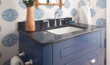 Navy quartz countertop colors with blue cabinet, blue patterned wallpaper, vase, bamboo mirror.