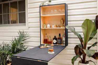 DIY outdoor Murphy ball folded down on wall and stocked with liquor and barware