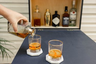Pouring whisky into two cocktail glasses set on tabletop of Murphy bar