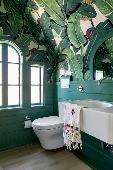 modern toilet in green bathroom with banana palm print wallpaper