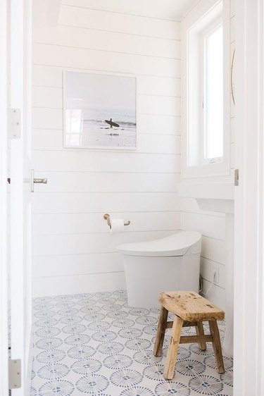 modern toilet in bathroom with white shiplap and pattern floor tiles