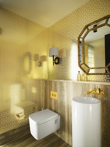 modern toilet in glam bathroom with gold wallpaper and brass mirror