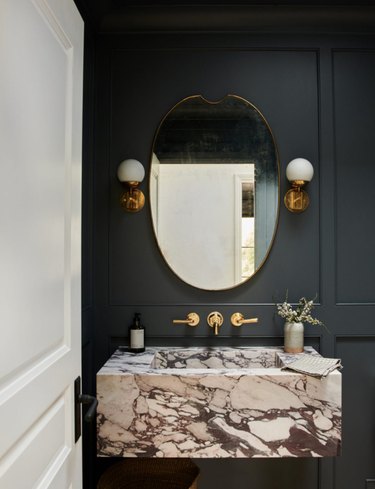 Bathroom with black walls, marble sink, mirror, sconces.