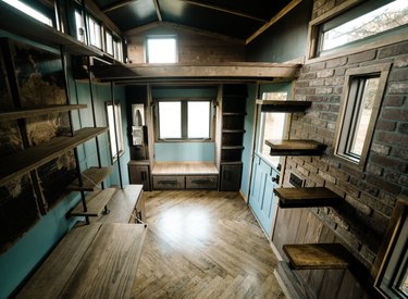 floating tiny house stairs in room with dark wood chevron pattern floors, brick walls, and open shelves