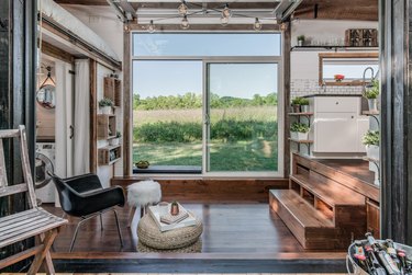 tiny house stairs and dark wood floors, black mid century modern side chair, pouf, sheepskin stool, wood chair, glass sliding door, white subway tile, white cabinets.