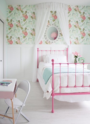 girls bedroom idea with pink bed frame and green patterned wallpaper above white wainscoting