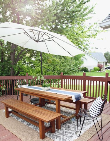 outdoor patio dining area with wood benches and table on top of area rug  with umbrella