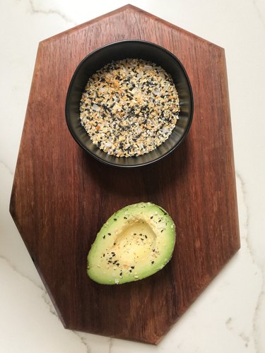 Wood board with spices in black bowl and avocado