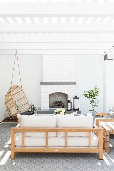 white outdoor patio seating area in front of fireplace with hanging chair and sofas