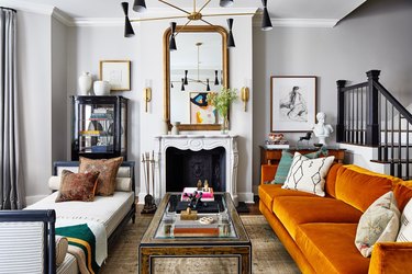 elegant living room with ornate traditional fireplace and mirror on top, orange sofa, white daybed