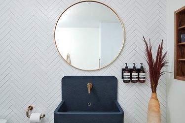 Navy bathroom sink idea with chevron tile backsplash and round mirror