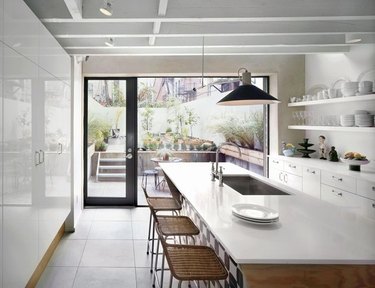 Floor-to-ceiling kitchen windows in modern kitchen with wood and white island and woven bar stools