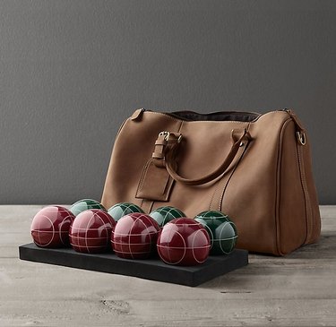 The bocce set next to a leather bag