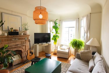 Living room with exposed brick fire place, plants, and bay window curtains