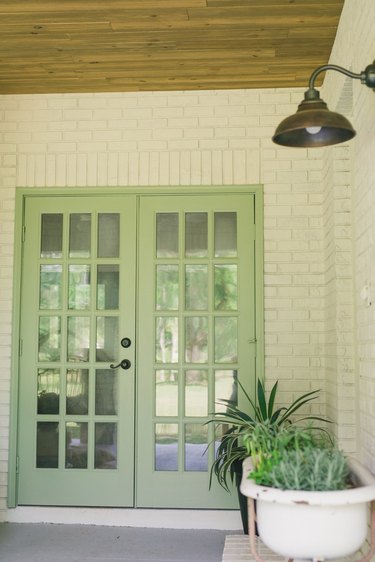 Patio French doors painted in sage color and surrounded by white brick