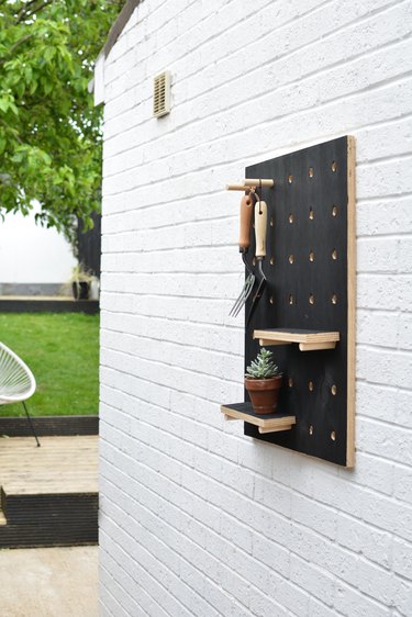 Painted black wooden pegboard with garden tools