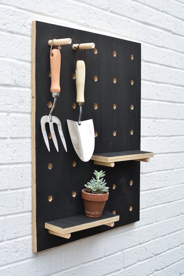 Black wooden pegboard with garden tools
