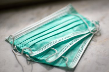 three green disposable face masks on a white marble countertop