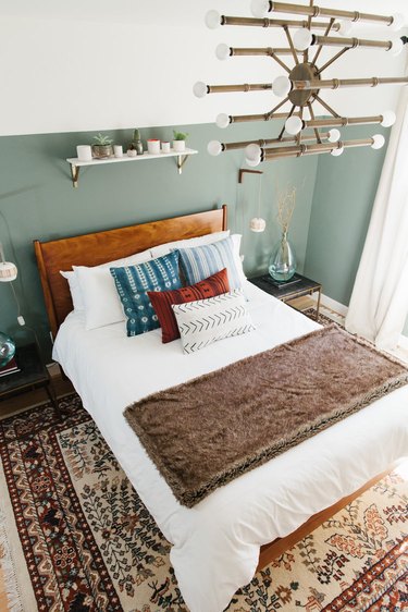 Bohemian guest room with a sage color accent wall and brass chandelier