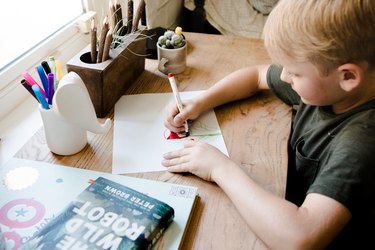 Young boy drawing with markers at his wood desk.
