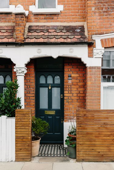 traditional brick home with white trim and potted plants at black front door