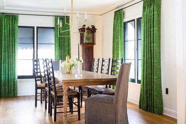 black windows in dining room with wood floors and green window treatments